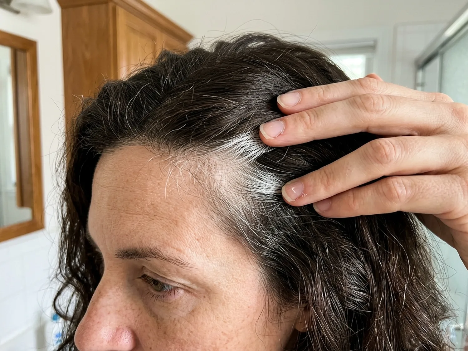 Close-up of a woman's fingers parting her dark hair at the temple to show bright white strands that stayed white after coloring